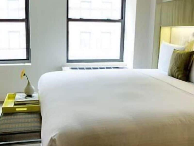 Stylish hotel room at The Shoreham Hotel featuring a comfortable bed, minimalist decor, and natural light from large windows.