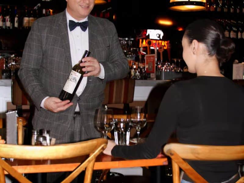 Sommelier presenting a wine bottle to a guest at a bar during a vintage wine tasting experience.