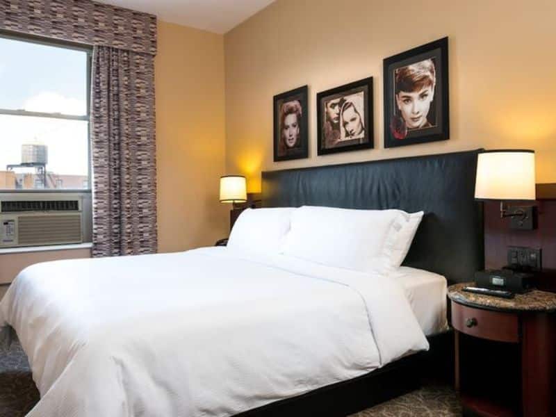 Cozy art deco-style hotel room at Washington Square Hotel featuring a queen bed, decorative wall art, bedside lamps, and window with city view.