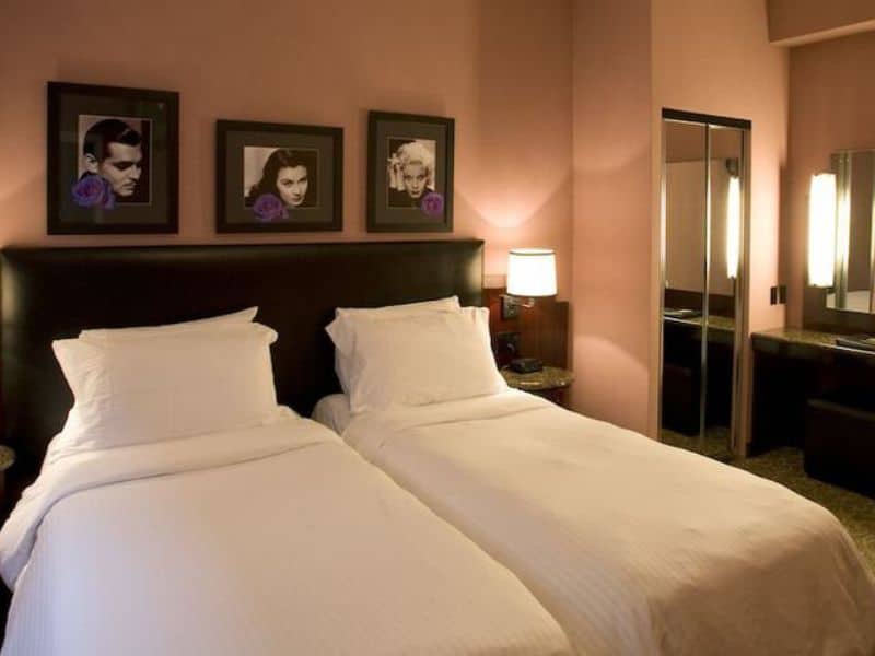 Cozy art deco-style hotel room with two twin beds, framed vintage portraits on the wall, and modern amenities, reflecting the European-inspired design of Washington Square Hotel.