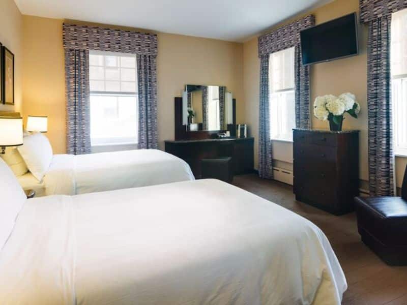Cozy art deco-style hotel room at Washington Square Hotel featuring two beds, natural light from windows, a dresser, and a flat-screen TV, highlighting comfort and European-inspired design.