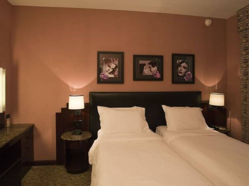 Cozy art deco-style hotel room at Washington Square Hotel featuring twin beds, framed artwork, bedside lamps, and modern furnishings.