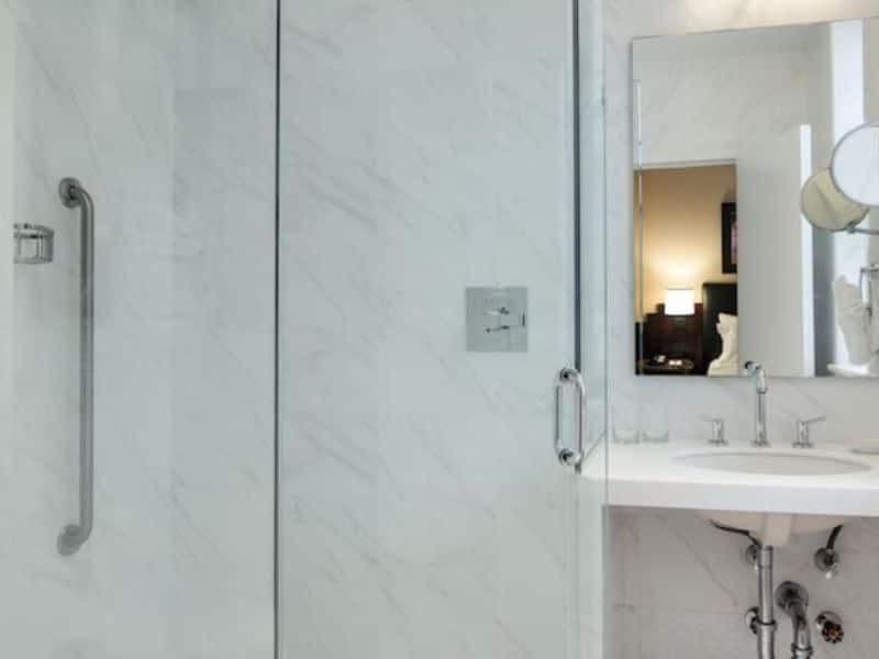 Modern hotel bathroom with glass shower, marble walls, and sink, reflecting European-inspired design of Washington Square Hotel amenities.