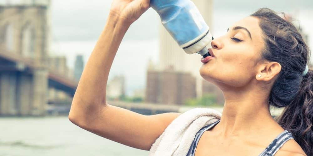 Woman drinking from a refillable water bottle in NYC, emphasizing hydration during summer heat and outdoor activities.