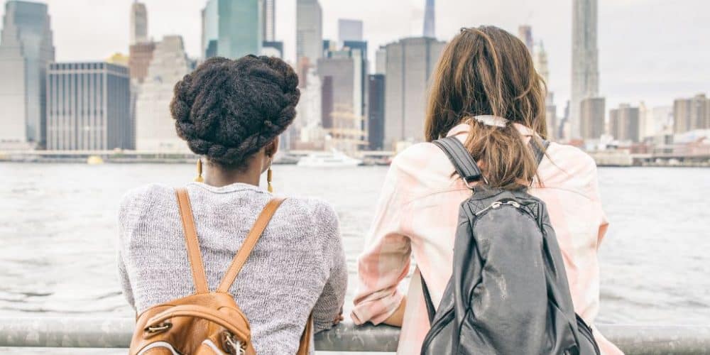 Two tourists overlooking the New York City skyline, showcasing backpacks and casual summer attire, embodying the ease of exploring the city.