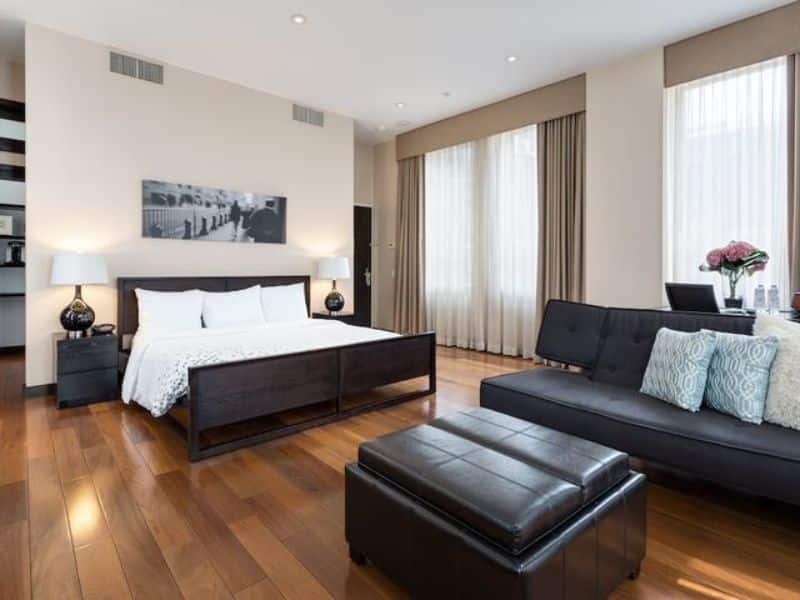 Modern hotel suite at Hotel 57 featuring a queen bed, lounge area with a sofa, hardwood floors, large windows with curtains, and a minimalist design.