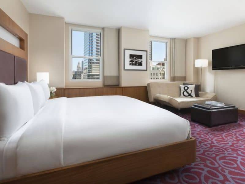 Modern hotel room at Hotel 57 featuring a king-sized bed, seating area with a sofa, large windows with city views, and a flat-screen TV, emphasizing comfort and convenience for travelers in Midtown Manhattan.