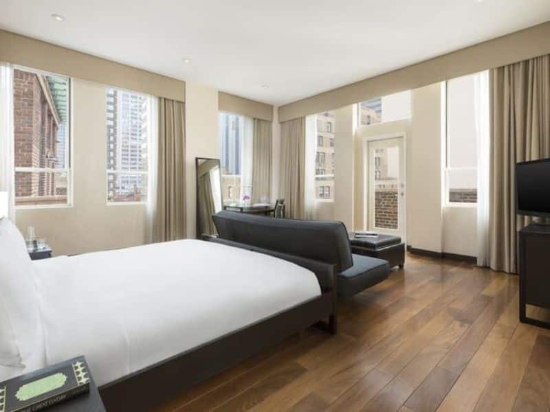 Modern hotel room at Hotel 57, featuring a king-size bed, large windows with city views, wooden flooring, and a seating area with a TV.