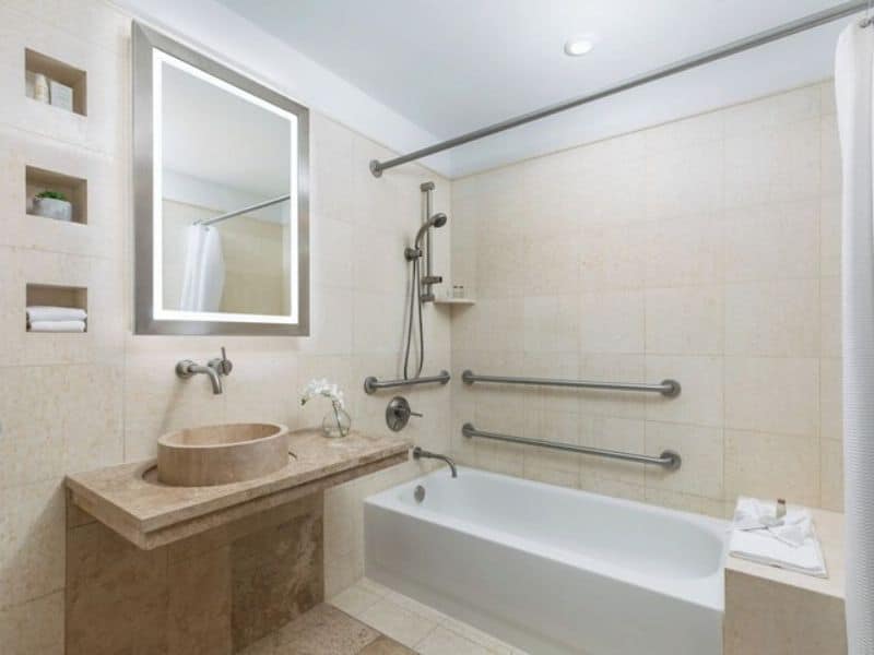 Modern accessible bathroom featuring a bathtub, grab bars, a sleek sink with a round basin, and a large mirror, highlighting Hotel 57's commitment to wheelchair accessibility and comfort.
