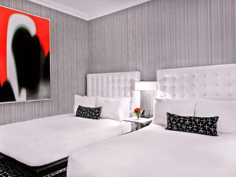 Modern hotel room with two beds, decorative pillows, stylish lamp, and abstract wall art, showcasing the contemporary design of the Moderne Hotel in New York City.