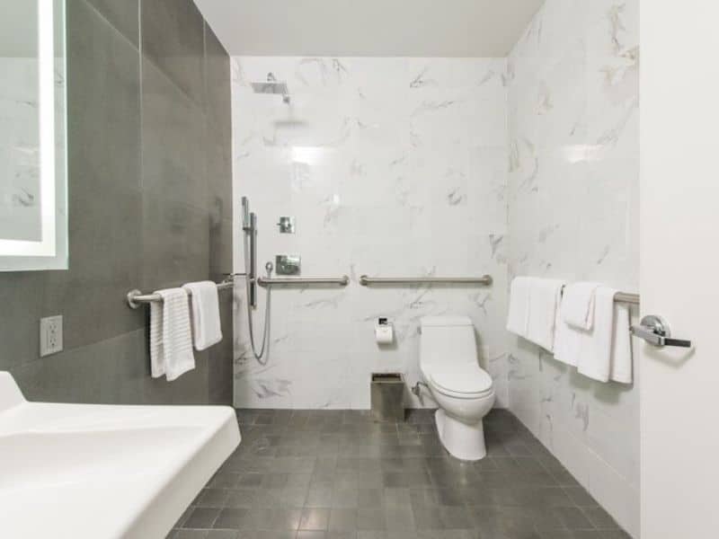 Modern hotel bathroom with accessible features, including grab bars, a walk-in shower, and a toilet, highlighting the Moderne Hotel's wheelchair accessibility.