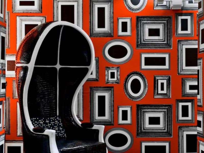 Black and white modern chair against vibrant orange wall adorned with various picture frames, reflecting the contemporary aesthetic of the Moderne Hotel in New York City.
