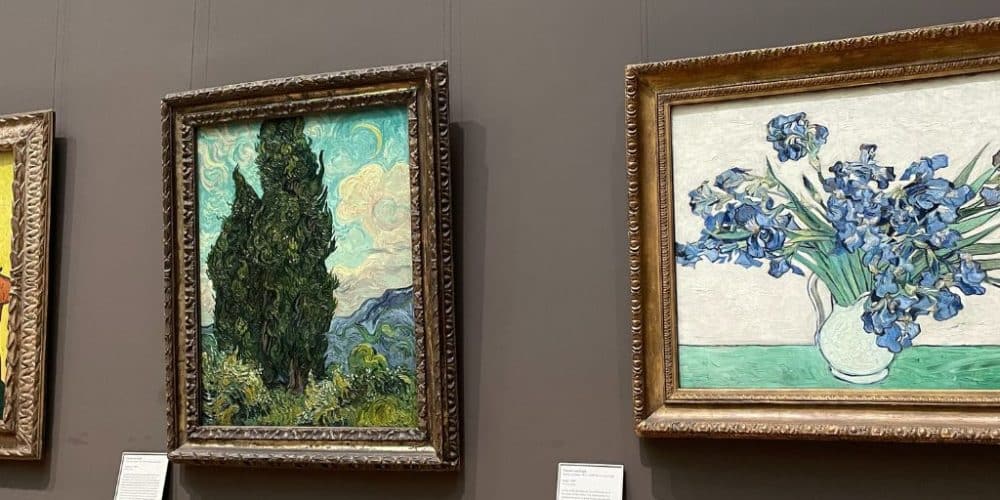 Vincent van Gogh paintings displayed in a New York City museum, featuring a cypress tree and a bouquet of irises, emphasizing the artistic culture and quiet exploration of the city.