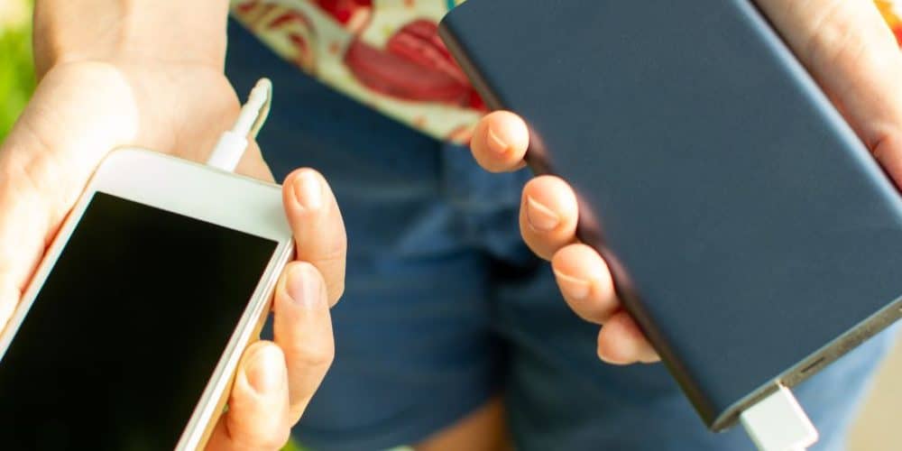 Person holding smartphone and power bank, illustrating essential travel accessories for summer trips to New York City.