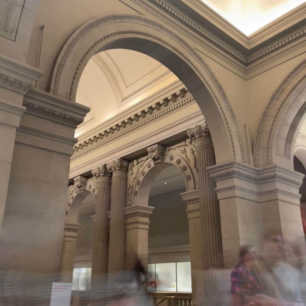 Architectural details of the Metropolitan Museum of Art in New York City, featuring grand arches and ornate columns, with blurred figures of visitors illustrating the vibrant atmosphere of cultural exploration.