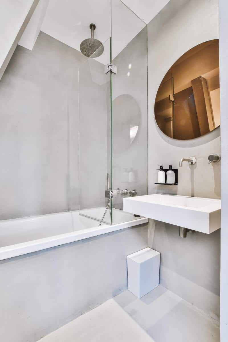 Modern hotel bathroom featuring a bathtub, glass shower enclosure, round mirror, and minimalist sink design, emphasizing family-friendly amenities and comfort.