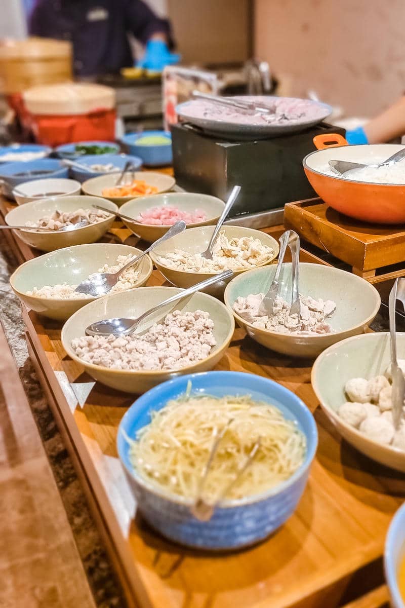 Breakfast buffet featuring various bowls of ingredients including meats, noodles, and toppings, highlighting hotel dining options in New York City.