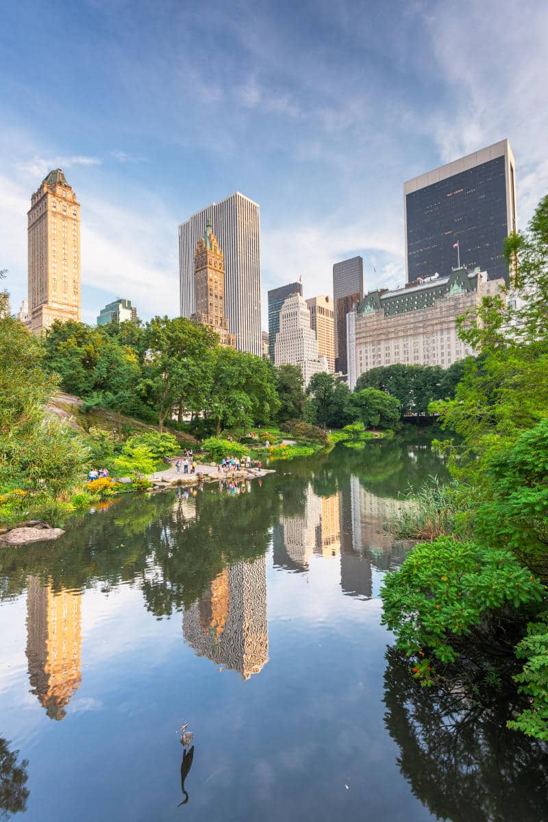 Central Park view with skyscrapers reflecting in the water, showcasing NYC's iconic skyline and lush greenery, highlighting a popular urban escape in Manhattan.