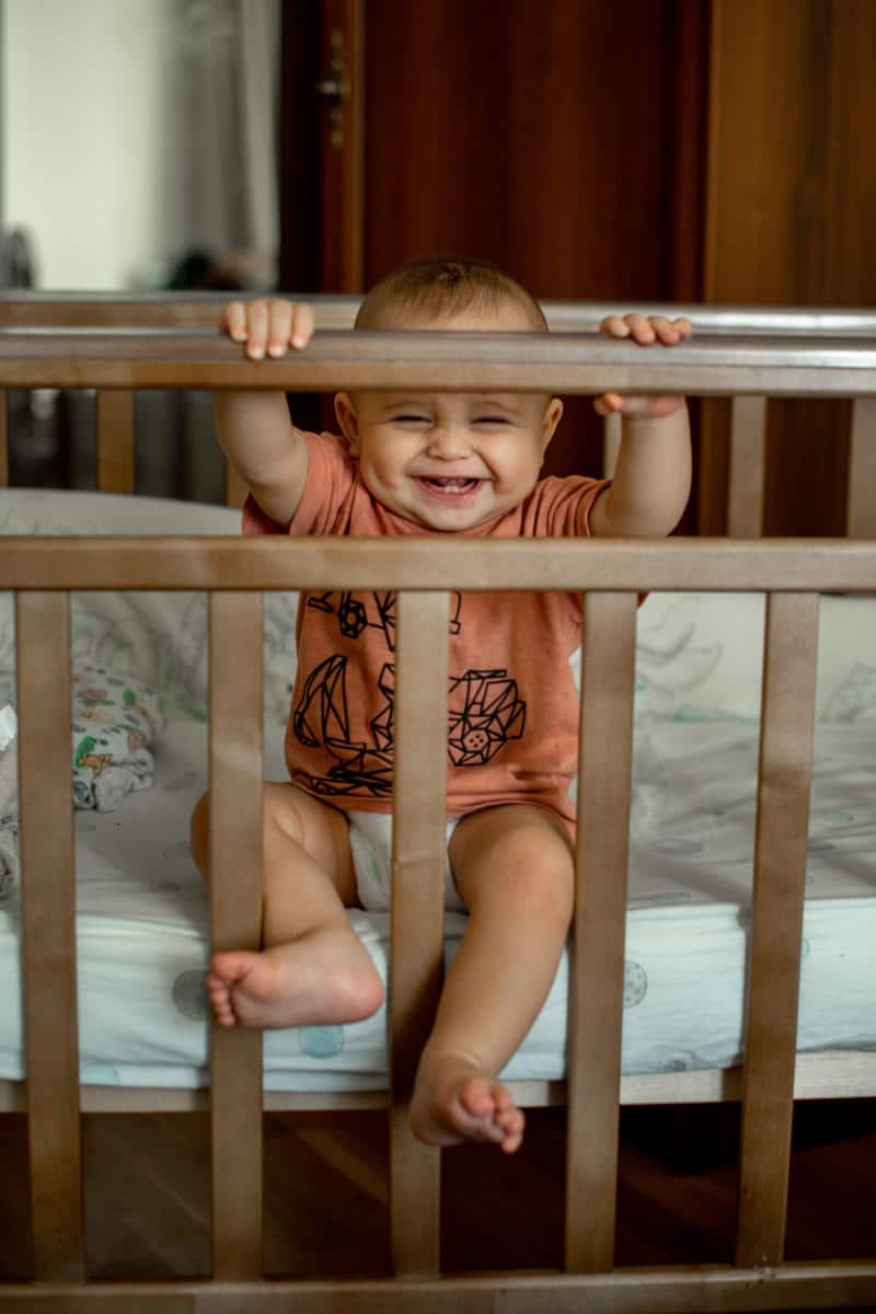 Smiling baby sitting in a crib, showcasing family-friendly accommodations and amenities for hotels in New York City.