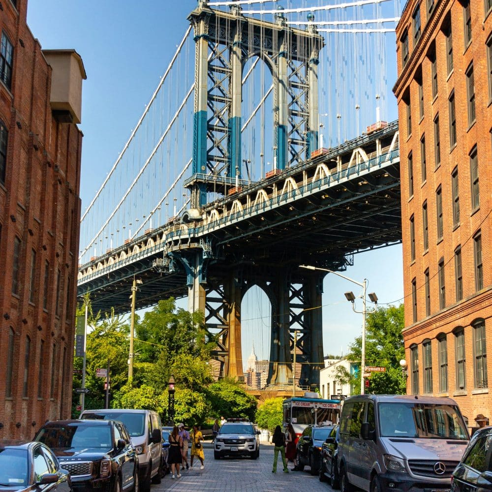 DUMBO neighborhood view featuring the Manhattan Bridge, cobblestone streets, and urban greenery, highlighting iconic photo angles and local architecture.