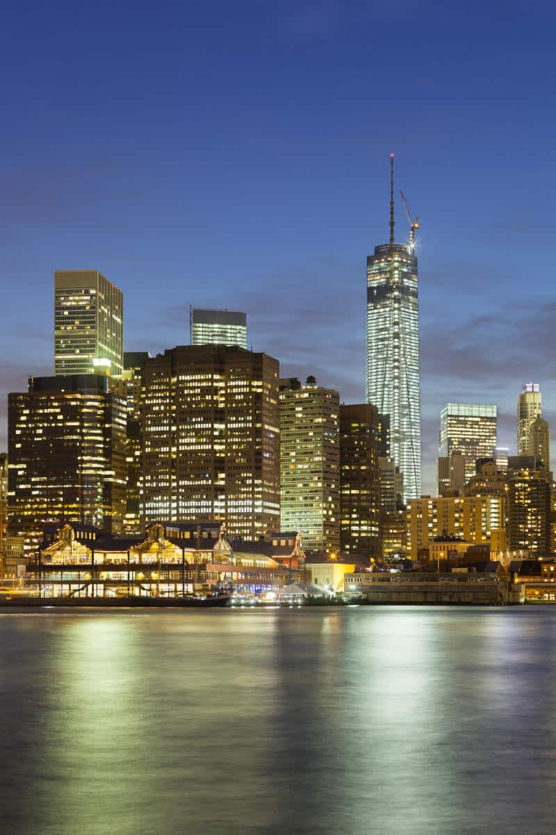 Manhattan skyline at night featuring One World Trade Center and illuminated buildings along the waterfront, representing iconic NYC landmarks.