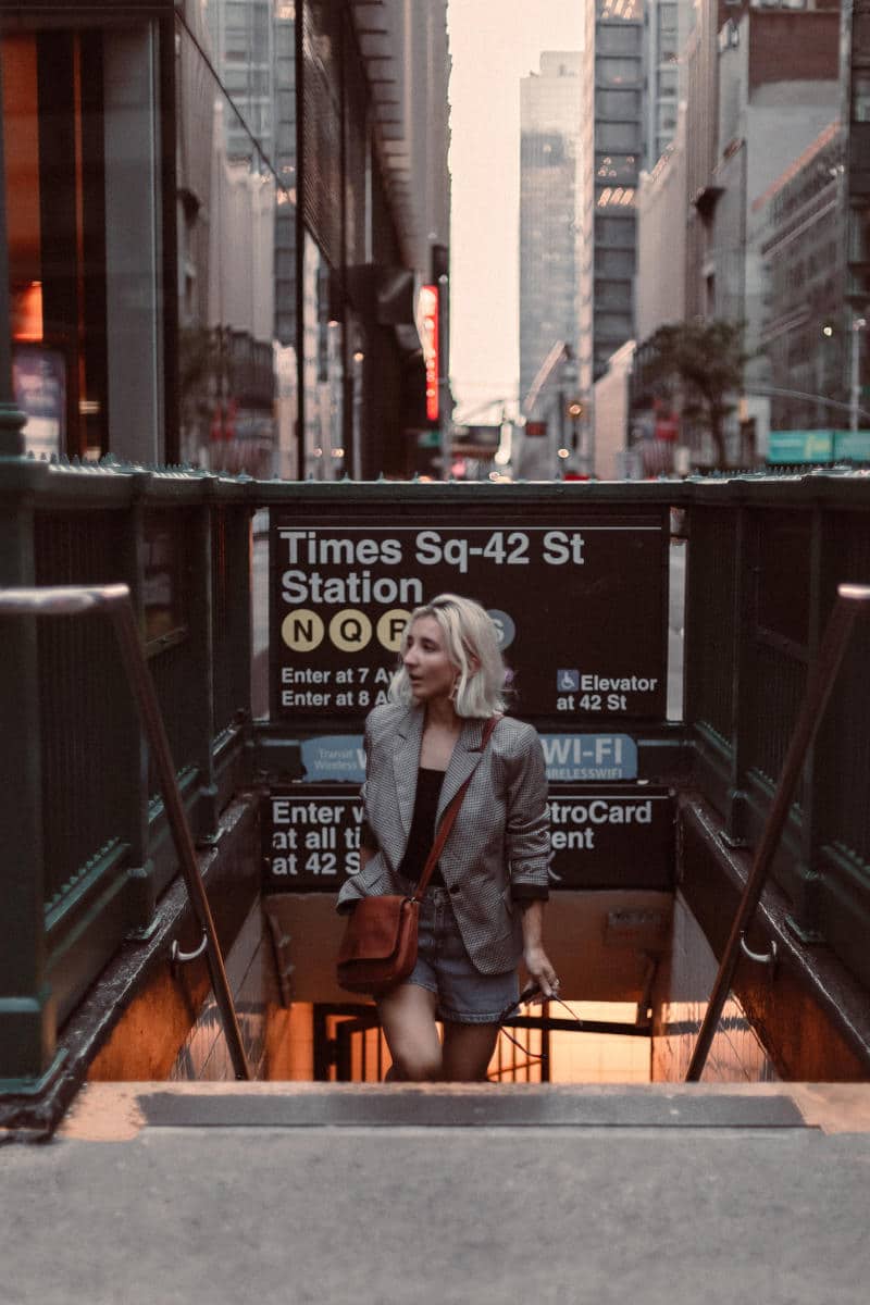Woman descending stairs at Times Square-42nd Street subway station, showcasing iconic NYC transit access in a bustling urban setting.