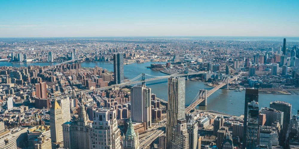 Aerial view of Lower Manhattan and Brooklyn, showcasing bridges and the harbor, emphasizing the iconic skyline and memorial context near One World Trade Center.